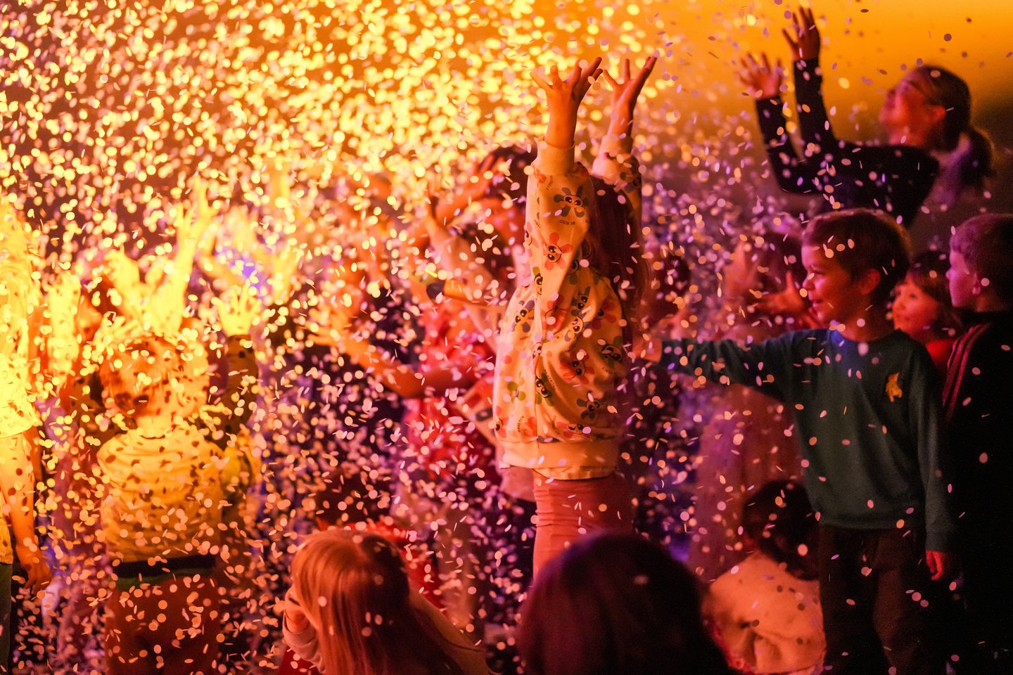Grupa dzieci na widowni. Na dzieci leci konfetti. Jedna z dziewczynek unosi wysoko ręce.