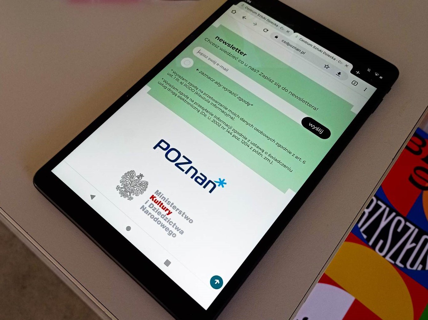 Tablet leżący na stole. Na tablecie wyświetlona jest informacja o newsletterze.