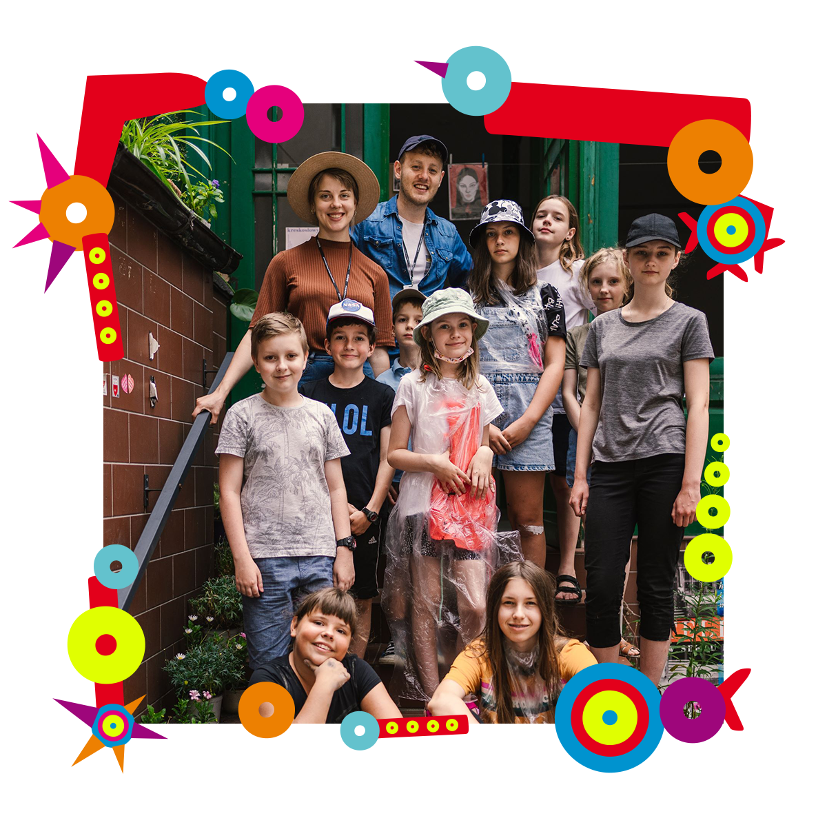 Grupa dzieci wraz z dwójką dorosłych pozuje do zdjęcia. Stoją na schodach przed budynkiem. Uśmiechają się. Niektóre osoby mają na głowach letnie kapelusze lub czapki z daszkiem. Dookoła zdjęcia kolorowa ramka.