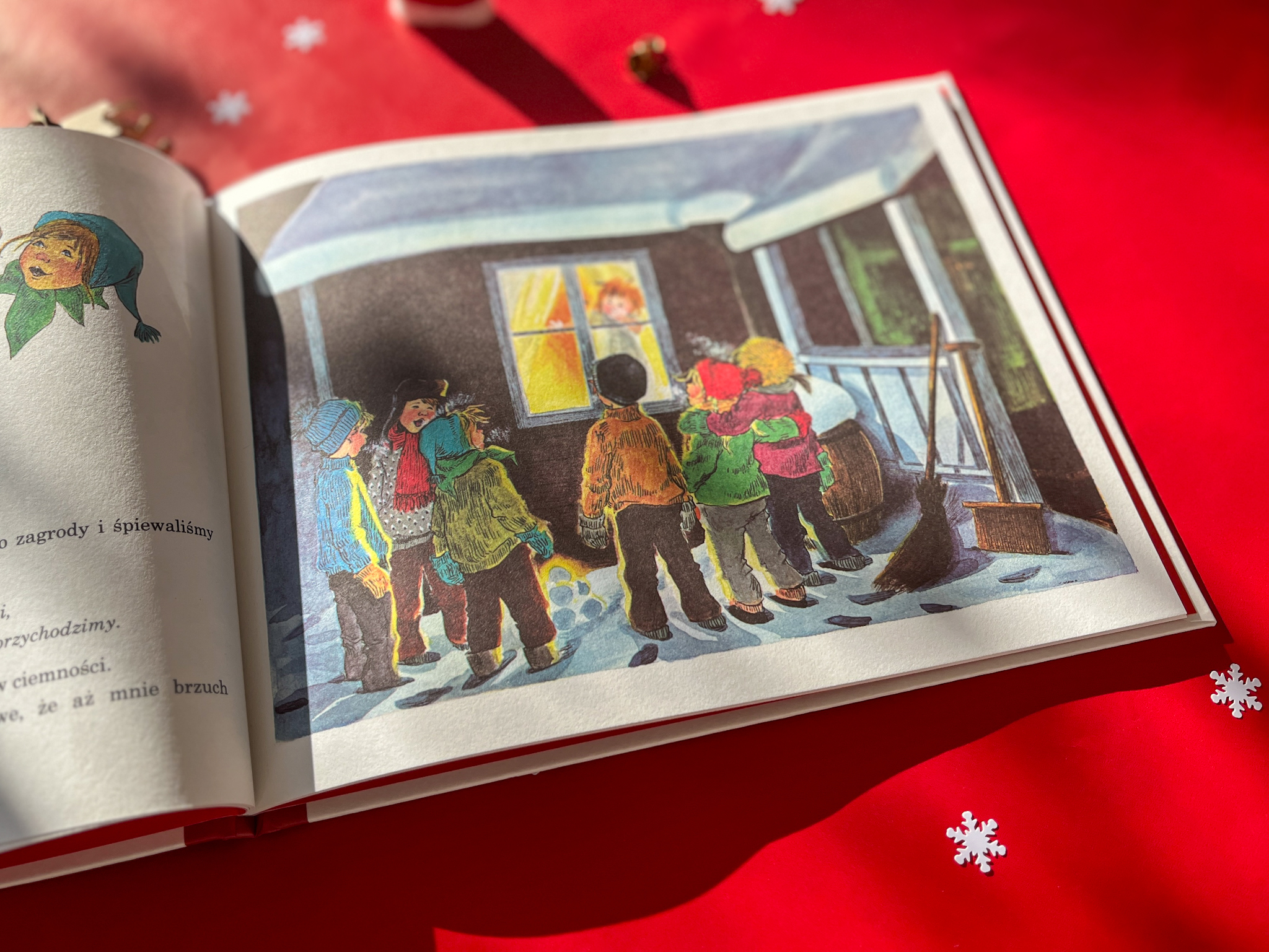 Otwarta książka ze świątecznymi ilustracjami leży na czerwonej tkaninie.